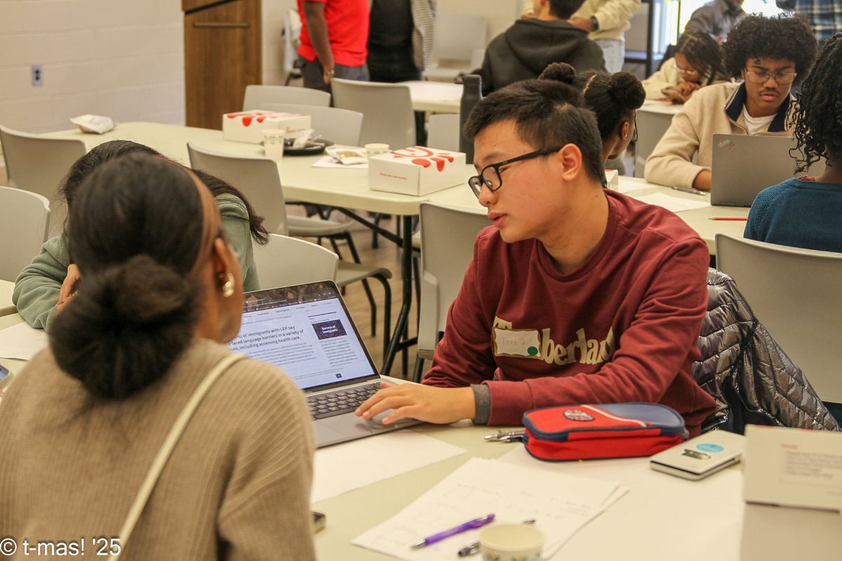 Two participants reviewing research on a laptop during a service learning hackathon session