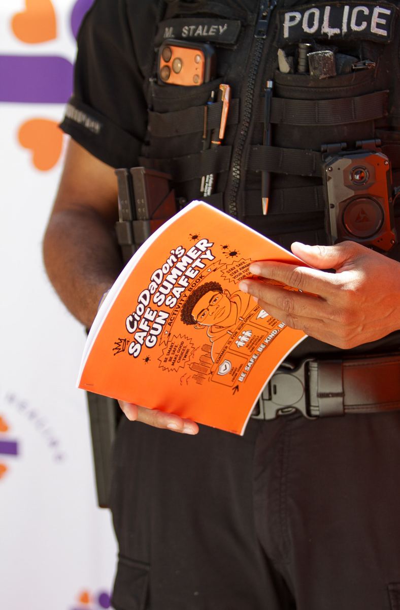 A public safety officer holding a youth gun-safety activity book at a Safe Summer community event